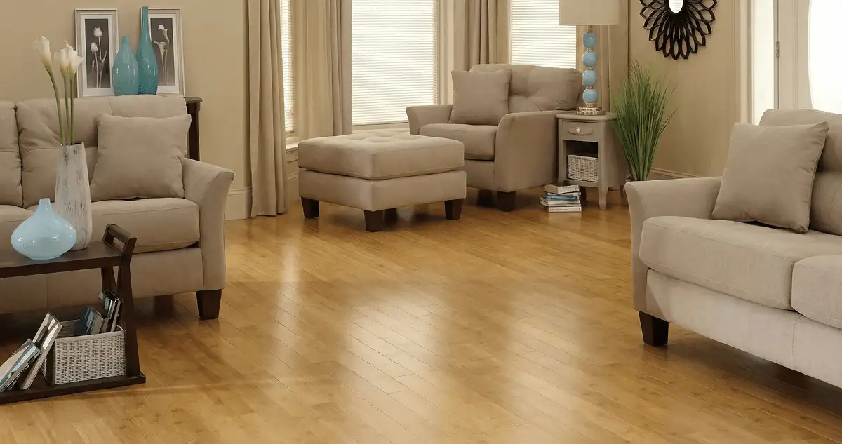 A living room with professionally installed bamboo flooring, beige sofas, a matching ottoman, a side table with a blue lamp, vases, framed pictures, and large windows with blinds and curtains in Tacoma, WA