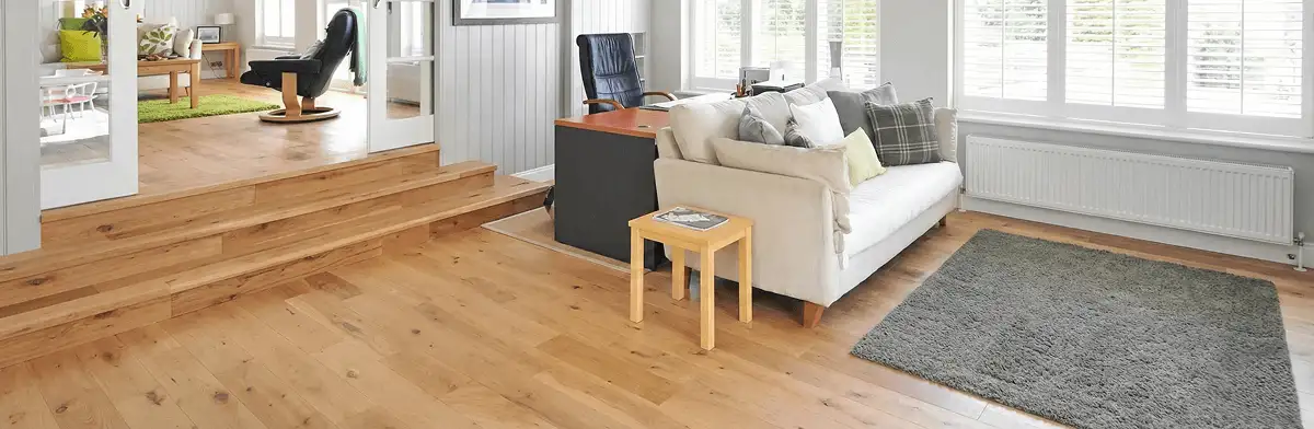 A modern living room with professionally installed laminate flooring, a beige sofa, a small side table, a gray rug, and large windows with white shutters in Tacoma, WA